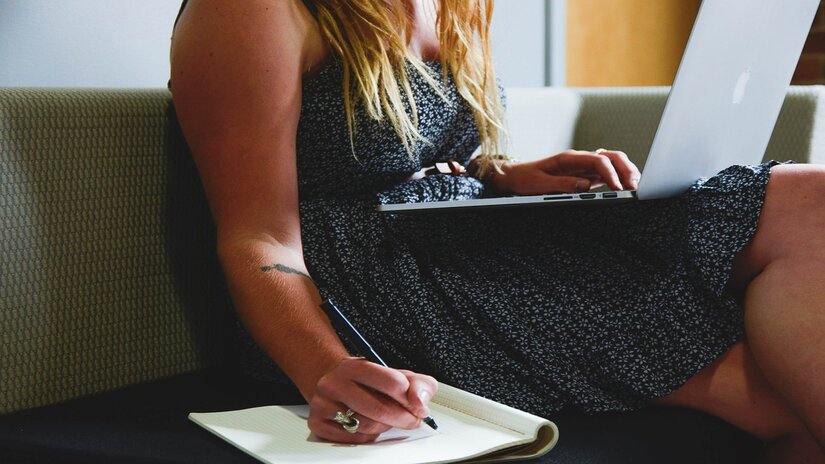 A woman sitting while writing and using her laptop